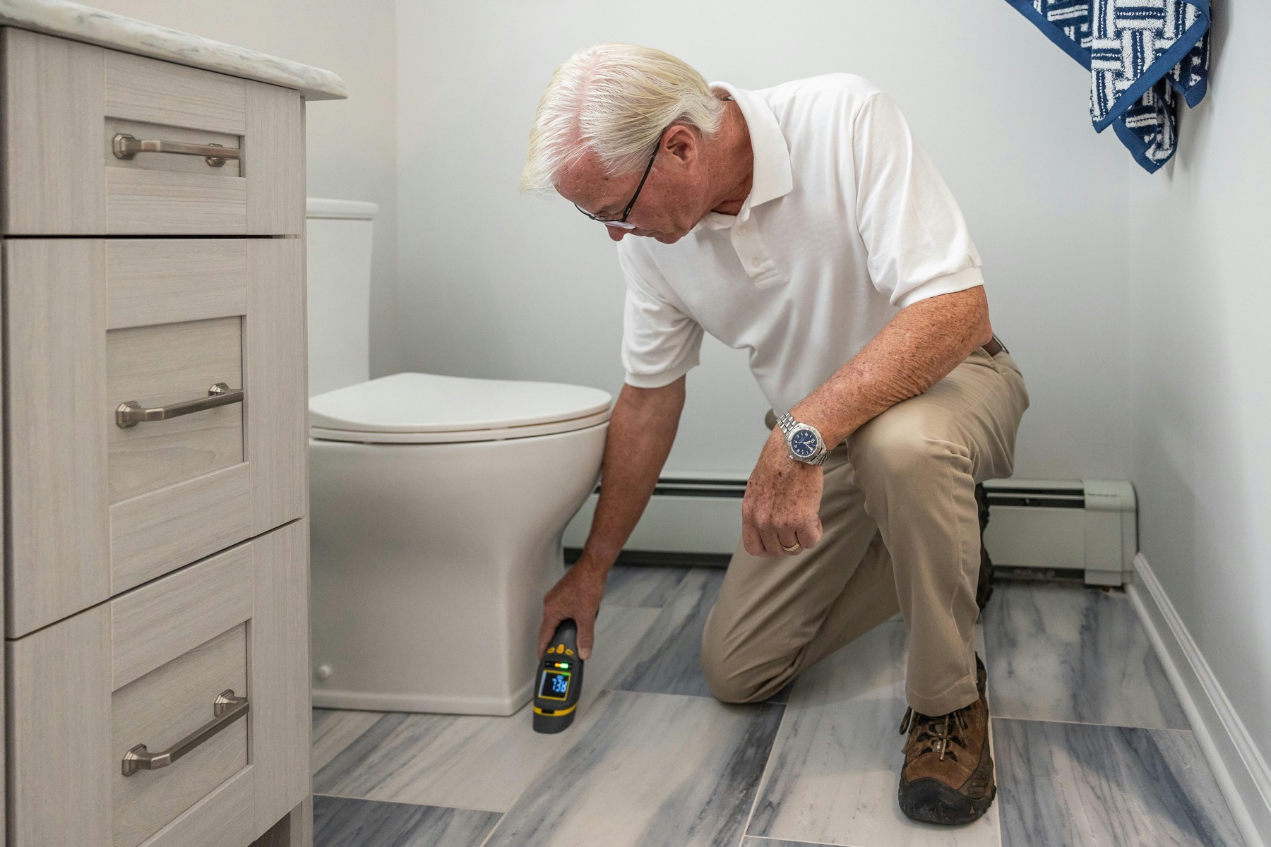 Technician using a moisture meter beside bathroom flooring